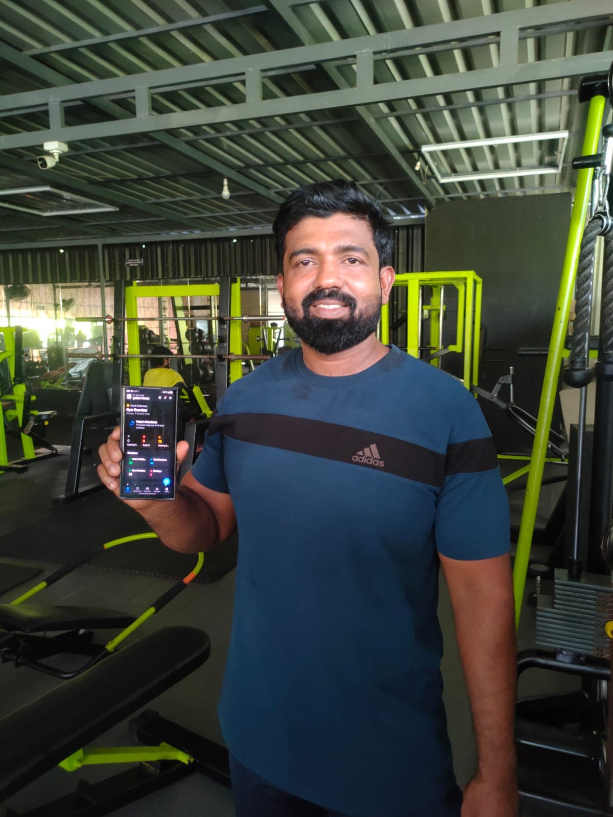 Shamnadh on the floor at Golden Fitness, holding his phone with the REPZ gym overview open.